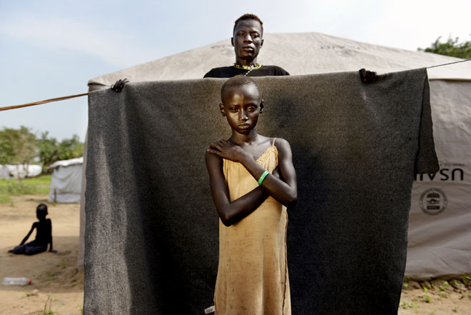 The instability that has been created by conflict in the newly independent South Sudan has impacted particularly on young women, especially those living in camps for IDPs. They risk and fear sexual violence while going about their daily lives, doing such things as collecting wood in the forest. Photographer Chris de Bode photographed and spoke to some of these girls at Minkaman refugee camp. They stand against a blanket that is held by people who play a significant role in their daily lives. The blanket symbolises the protection that these girls need. Outside this protected area is unsafe because of the fear of sexual violence and especially the fear of a future without security and peace. However, they are not alone as there are safe shelters where they can go to share their stories and get support and community workers to identify vulnerable families and offer help. Anoel, aged about seven: 'I don't know my age. I think I am seven years old, but it's not important. I don't feel safe, especially when I think of all the violence I saw. I am also afraid that people will think less of me because I am wearing a shirt that doesn't really cover my body. They will think I am poor.'